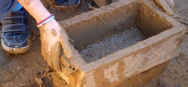 Mans que treuen un rectangle de fusta que ha servit per fer una peça de construccióde de palla i fang