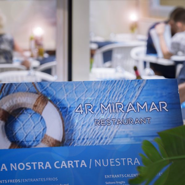 Primer pla de la carta del restaurant de l'hotel 4r Miramar amb el restaurant de fons