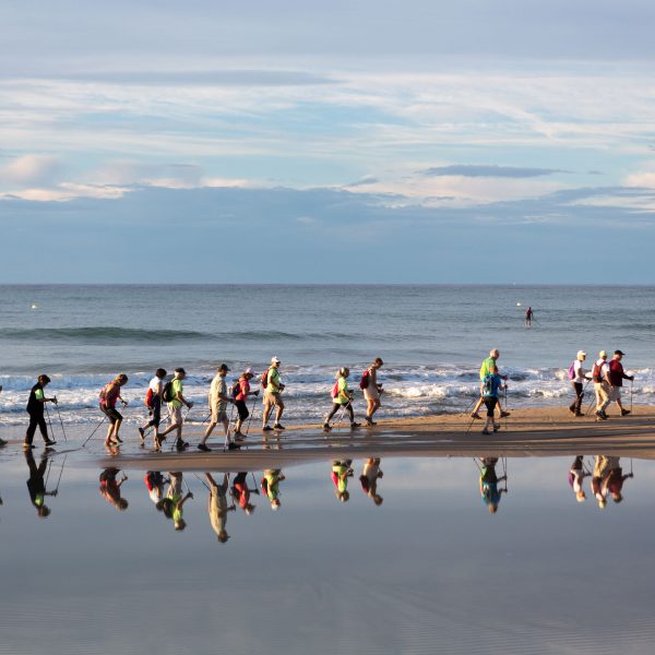 Grup de persones practicant marxa nòrdica a la platja