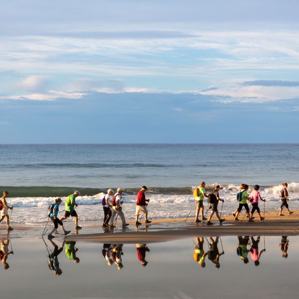 Grup de persones practicant marxa nòrdica caminen per la platja